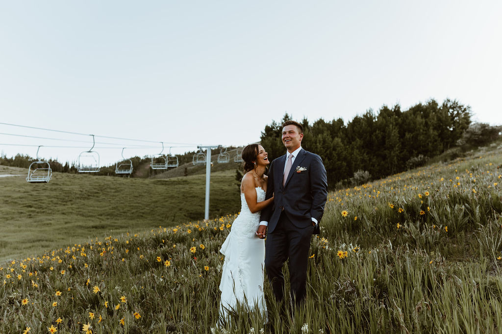 Couple standing in field of yellow wildflowers with chair lift in the background